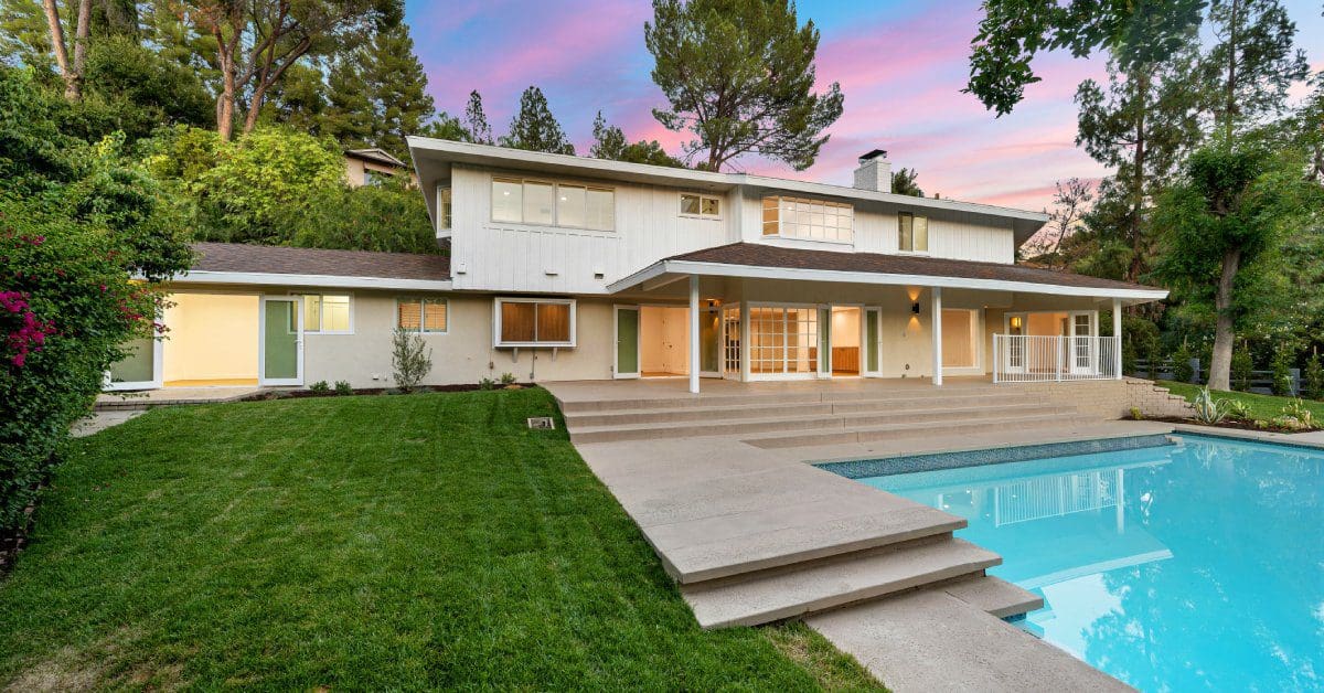 A spacious residential backyard with a pool and grassy area at a beige mid-century modern two-story home.