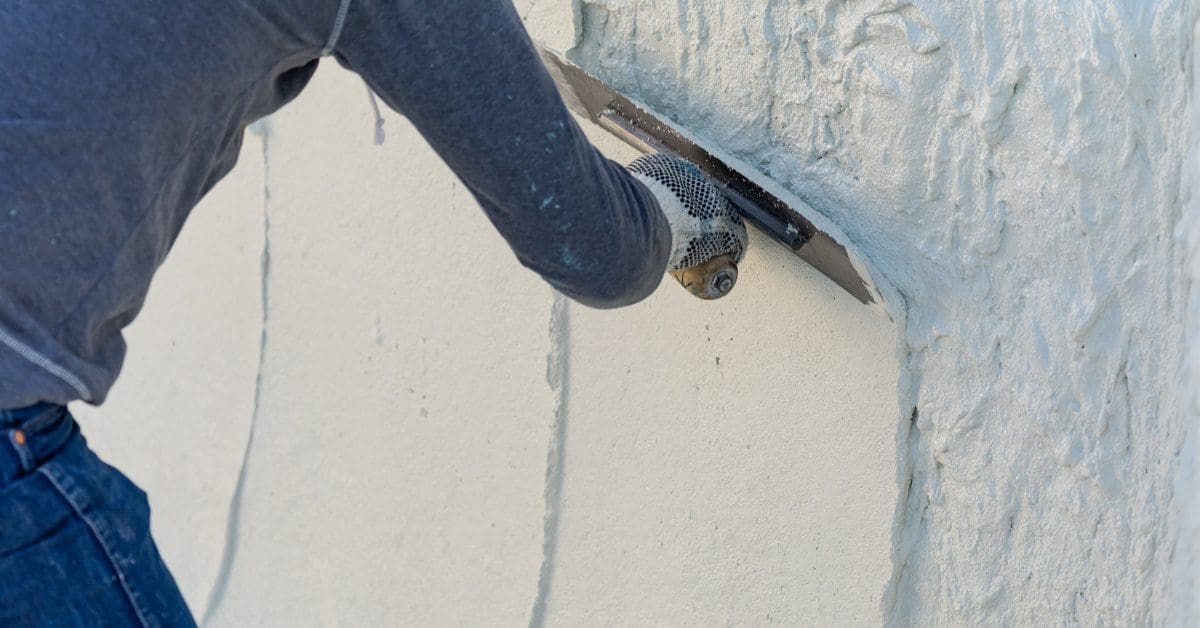 A close-up of a worker's smoothing wet pool plaster with a trowel. The worker is wearing protective gloves.