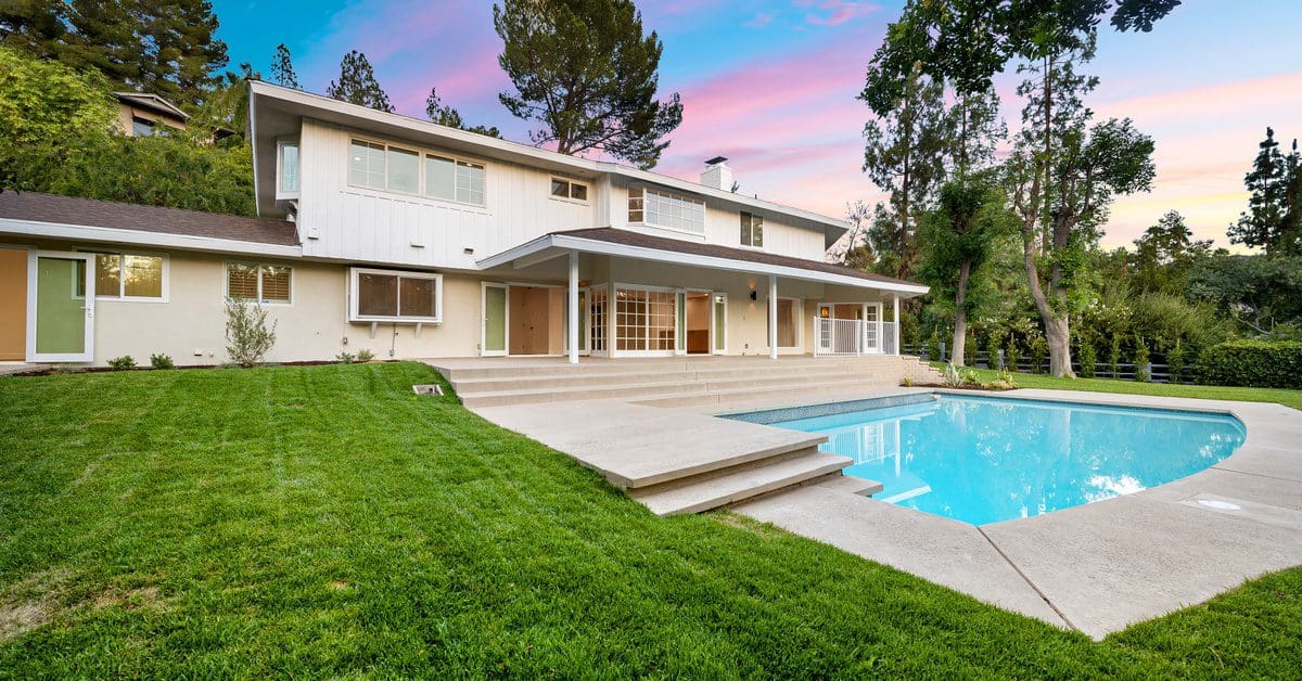 A luxurious remodeled pool in the backyard. The grass is freshly cut, and the landscaping is newly manicured.